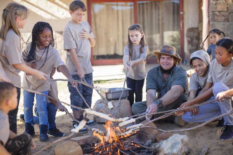 Kids roasting marshmellows by fire at summer camp