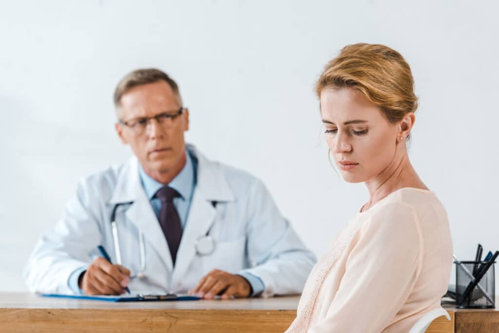 a sad woman sitting near doctor in white coat