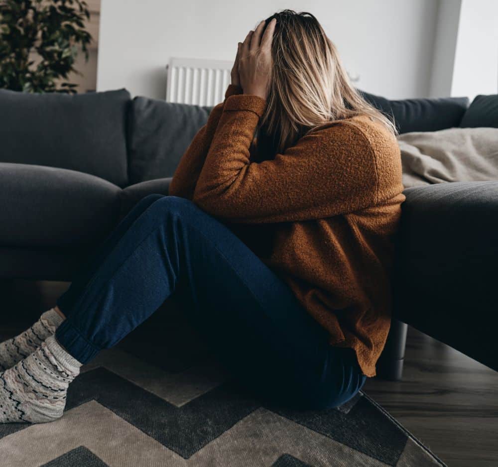 Woman sitting on floor with her hands over her face