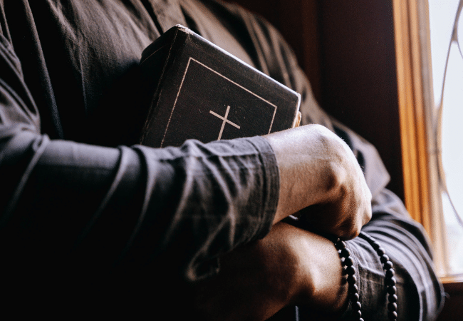 Illustrative image accompanying an article about Father Robert Carpentier, a former Diocese of Providence priest who admitted to sexually abusing a 13-year-old boy in Rhode Island. The image shows a priest holding a Bible and rosary beads.